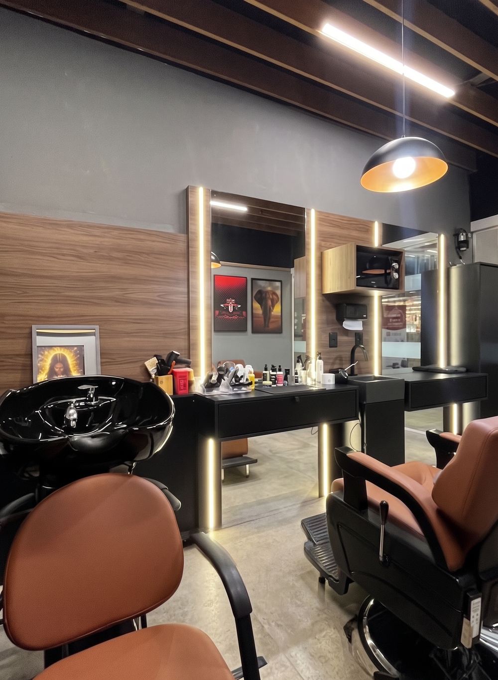 Estação de atendimento da Mr. Franklin Barbearia, com espelhos, iluminação âmbar e cadeiras de couro